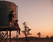 2 ringers sitting on a water tower having quiet drink while looking at the sunset
